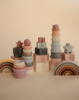 The mushie Stacking Rings Toy is shown upright on a beige background, featuring soft pastel colors like pink, brown, and cream. The non-toxic baby toy has ring shapes and promotes safe, stylish play.