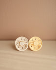 Lifestyle image of the Cream and Pale Daffodil Moon Silicone Frigg pacifiers.