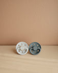 Lifestyle image of the Powder Blue and Slate Moon Silicone Frigg pacifiers.