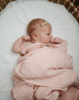Lifestyle image of a baby swaddled in organic cotton swaddle in Rose Vanilla