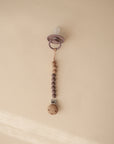 The mushie Silicone Pacifier Clip | Eva features alternating wooden and food-grade silicone beads in purple and is shown against a beige background—an adorable addition to your pacifier accessories collection.