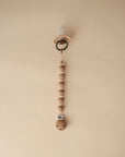 The mushie Silicone Pacifier Clip | Luna in beige features food-grade silicone and wooden beads, displayed vertically on a plain light tan background.