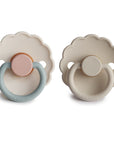 The FRIGG Daisy Natural Rubber Pacifier 2-Pack by FRIGG includes two rubber pacifiers with scalloped edges, one in pink and blue, the other in beige. Both have "FRIGG" embossed on the handle and natural rubber latex nipples, shown on a white background.