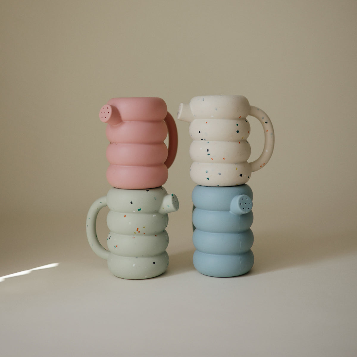 Four stackable Mushie Silicone Watering cans in pastel colors, two with a confetti pattern.