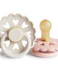 Product image of two Frigg Andersen Rubber baby pacifier, one Cream with heart designs and the other Blush, on a white background.