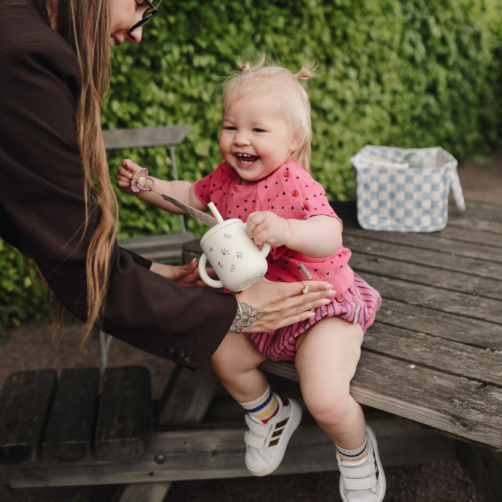 Toddler on bench reaches for teapot beside a mushie Diaper Caddy.