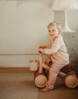 Smiling toddler in pink rides a mushie Mini Toddler Bike tricycle indoors.
