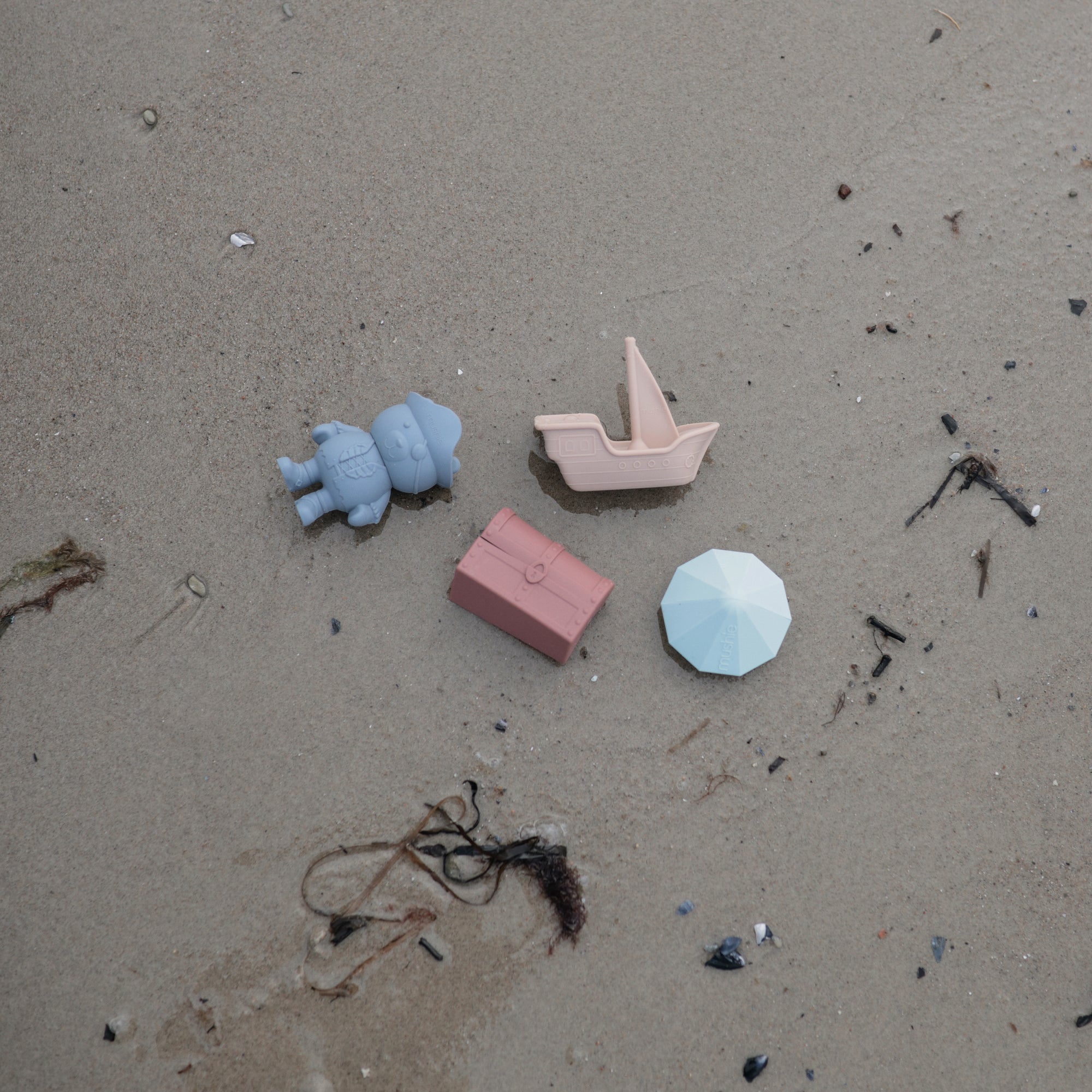 Lifestyle image of the mushie Pirate Bath Play Set toy son a sandy ground. 