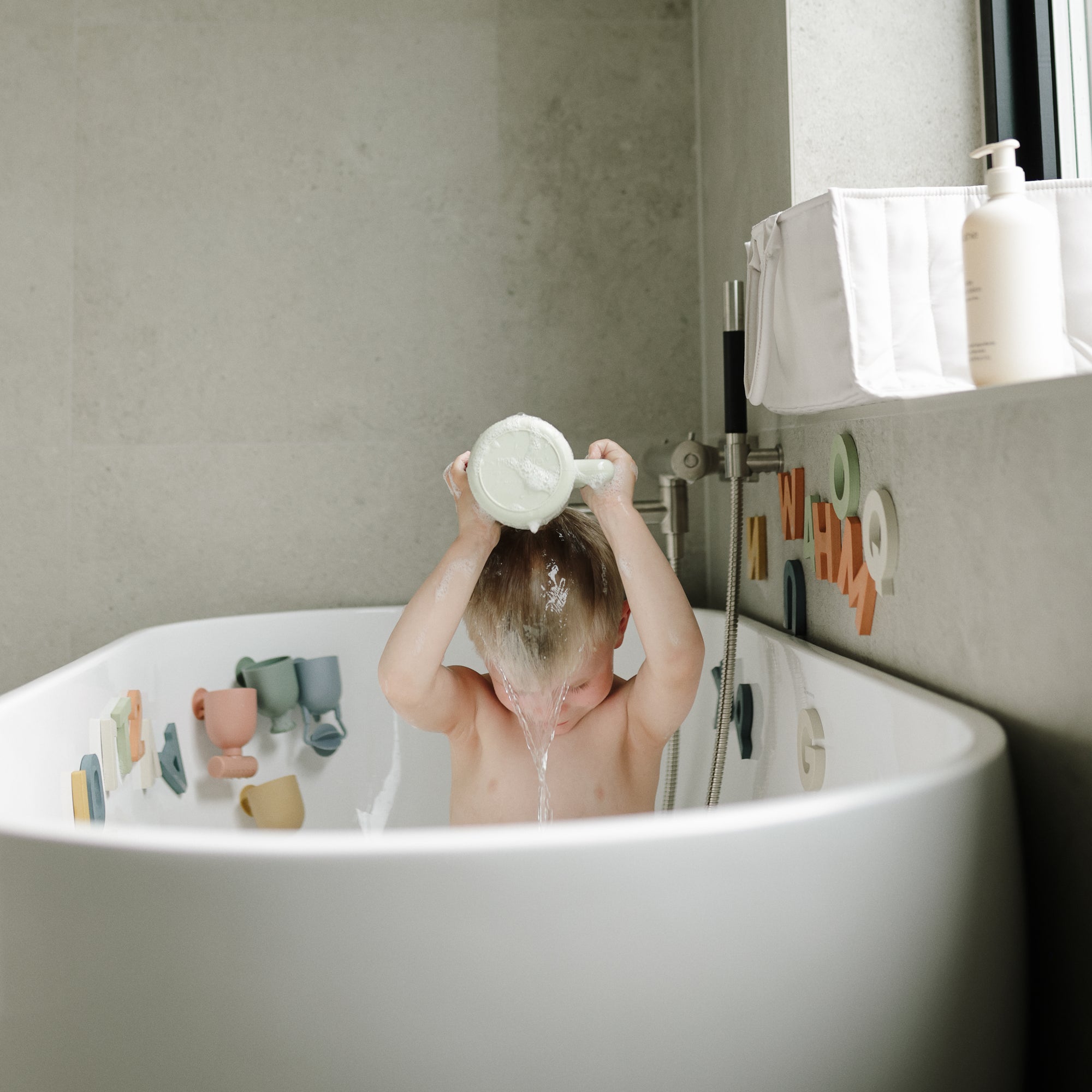 A child enjoys sensory fun in the tub with the mushie Pour and Play Bath Set.