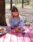 A young girl plays with Mushie Whale Bath Stackers on a pink table in a sunny park.