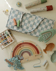 A soft play mat with pastel toys, a rattle, rainbow puzzle, and mushie Diaper Caddy nearby.