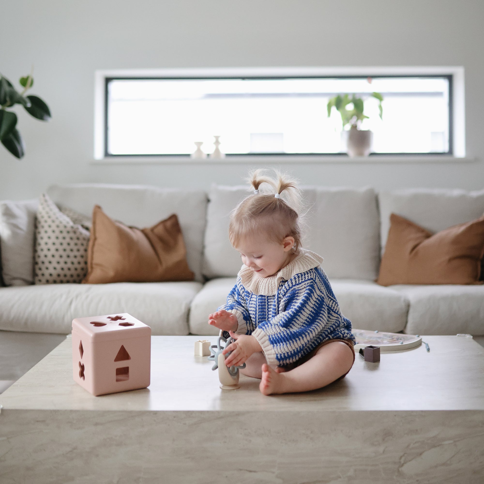Child playing with shape blocks and a suction spinner ball toy on a coffee table in a living room.