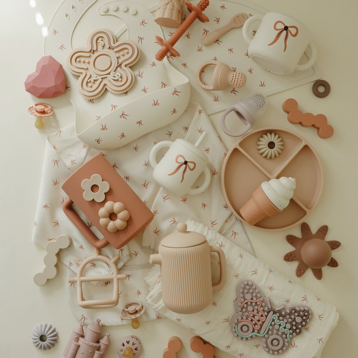 Mushie Silicone Sensory Toy with pastel baby cups and plates on a cream-colored surface.