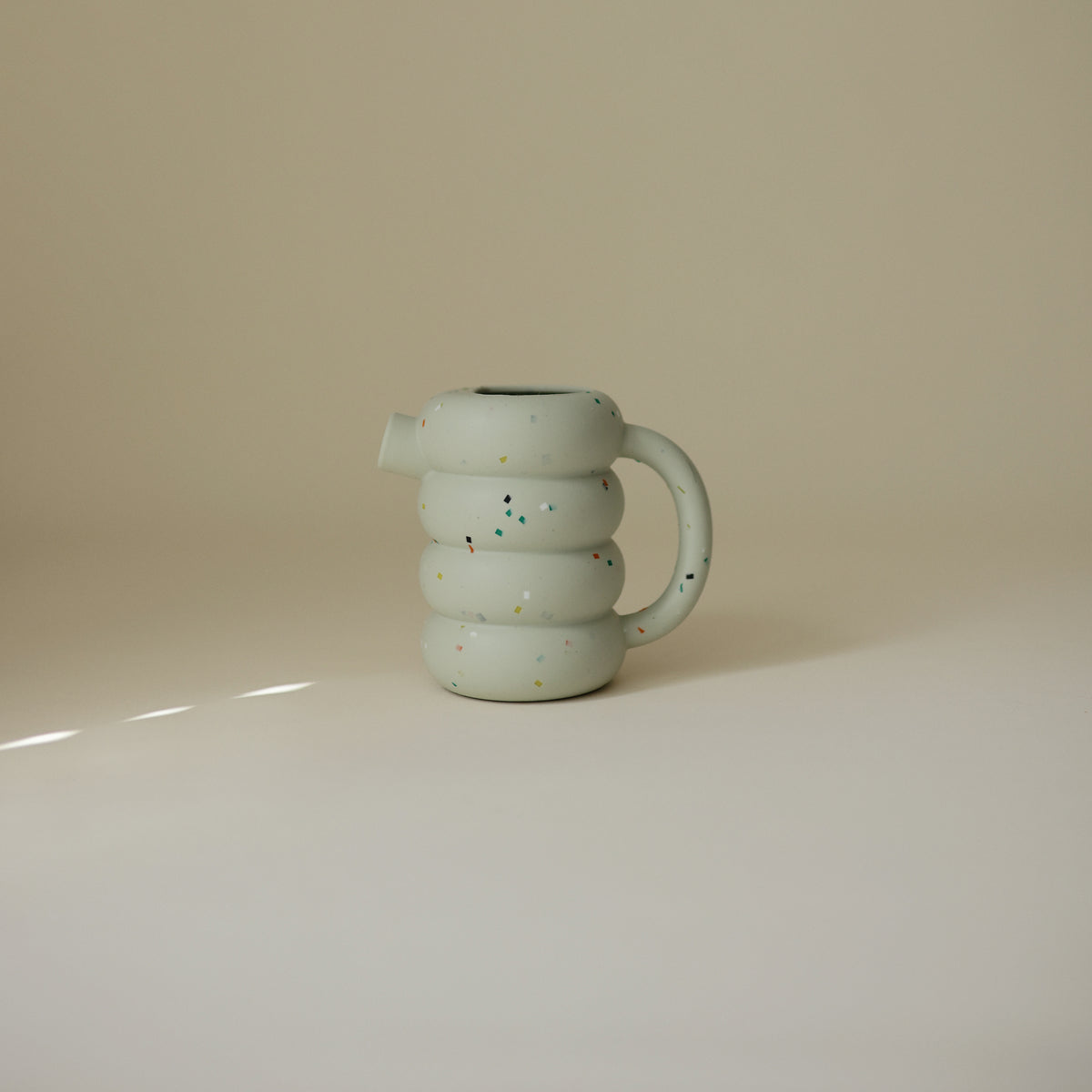 Light green, ribbed Mushie Silicone Watering Can for water play with colorful speckles.