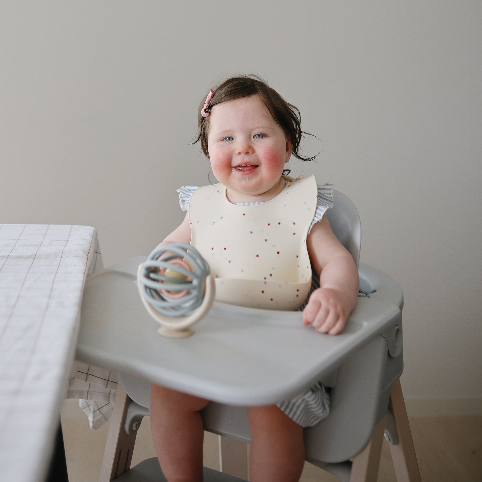 Child in a high chair with a suction spinner ball toy, sitting on a neutral background