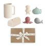 The mushie Sealife Bath Essentials Kit includes a ribbed beige mug, four silicone sea toys (bear in goggles, green submarine, pink octopus, grey whale), and a beige napkin holder, all packed in a brown gift box with a white ribbon.