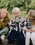 Three kids outdoors, two knitting, one with a Mushie Silicone Training Cup + Straw, all smiling.