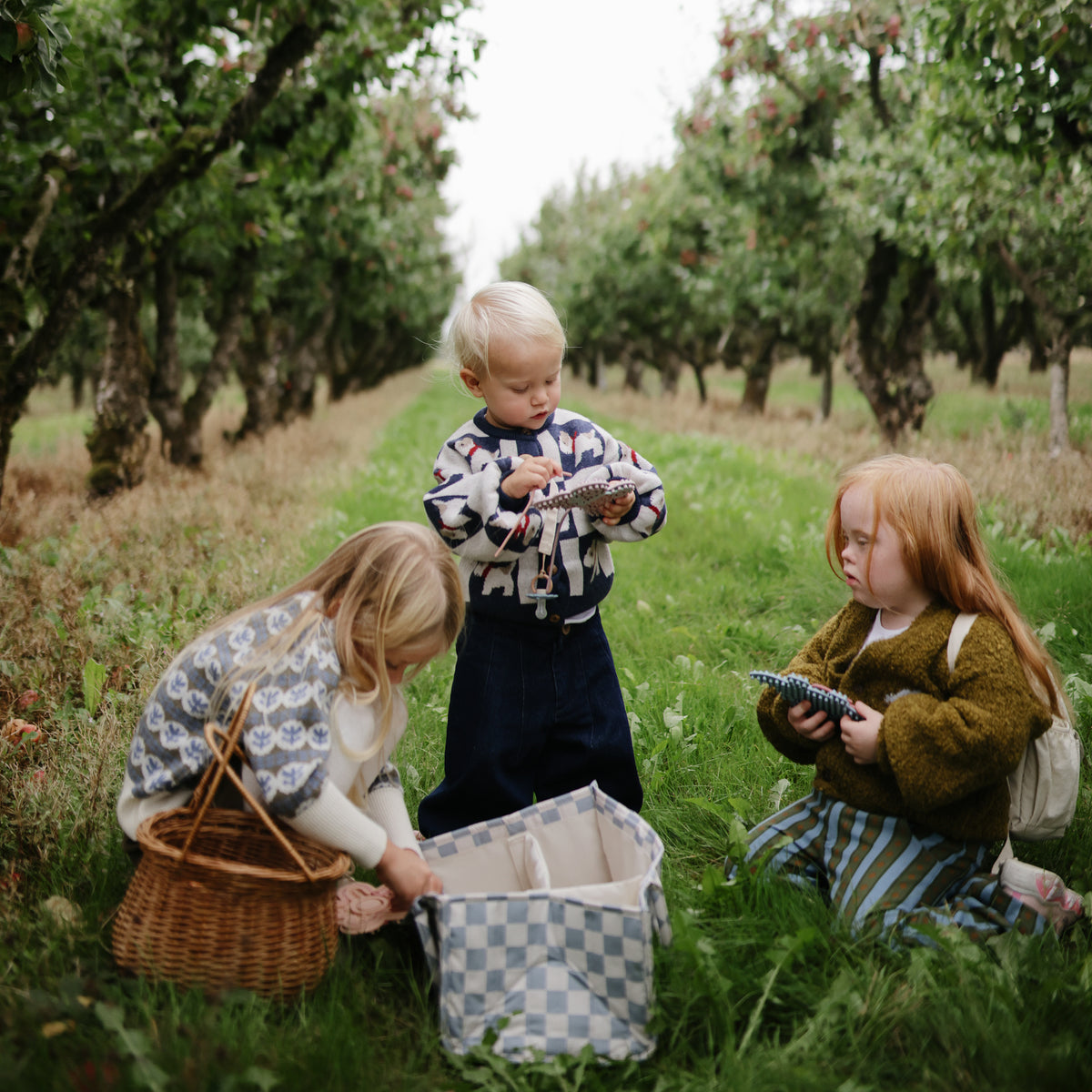 Three kids enjoy fine motor play with mushie’s Silicone Sensory Toy as they gather apples.