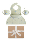 The mushie Bluey Gift Set includes a sage green silicone baby mealtime set with a bib, two cups, and a bowl featuring small animal prints, all displayed above a brown gift box tied with a cream ribbon.