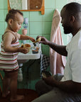 A man and toddler play with Mushie Whale Bath Stackers by the bathroom sink.