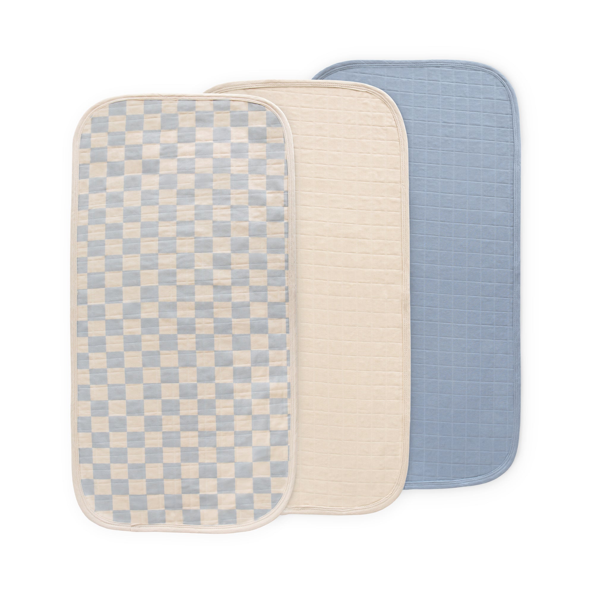 Three Mushie Changing Pad Liners—checkered, beige, and blue—overlapping each other.