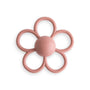 The mushie Daisy Rattle Teether is a pink, flower-shaped baby toy with six textured petals, a smooth round center embossed with "mushie," and a charming daisy design—perfect for teething.