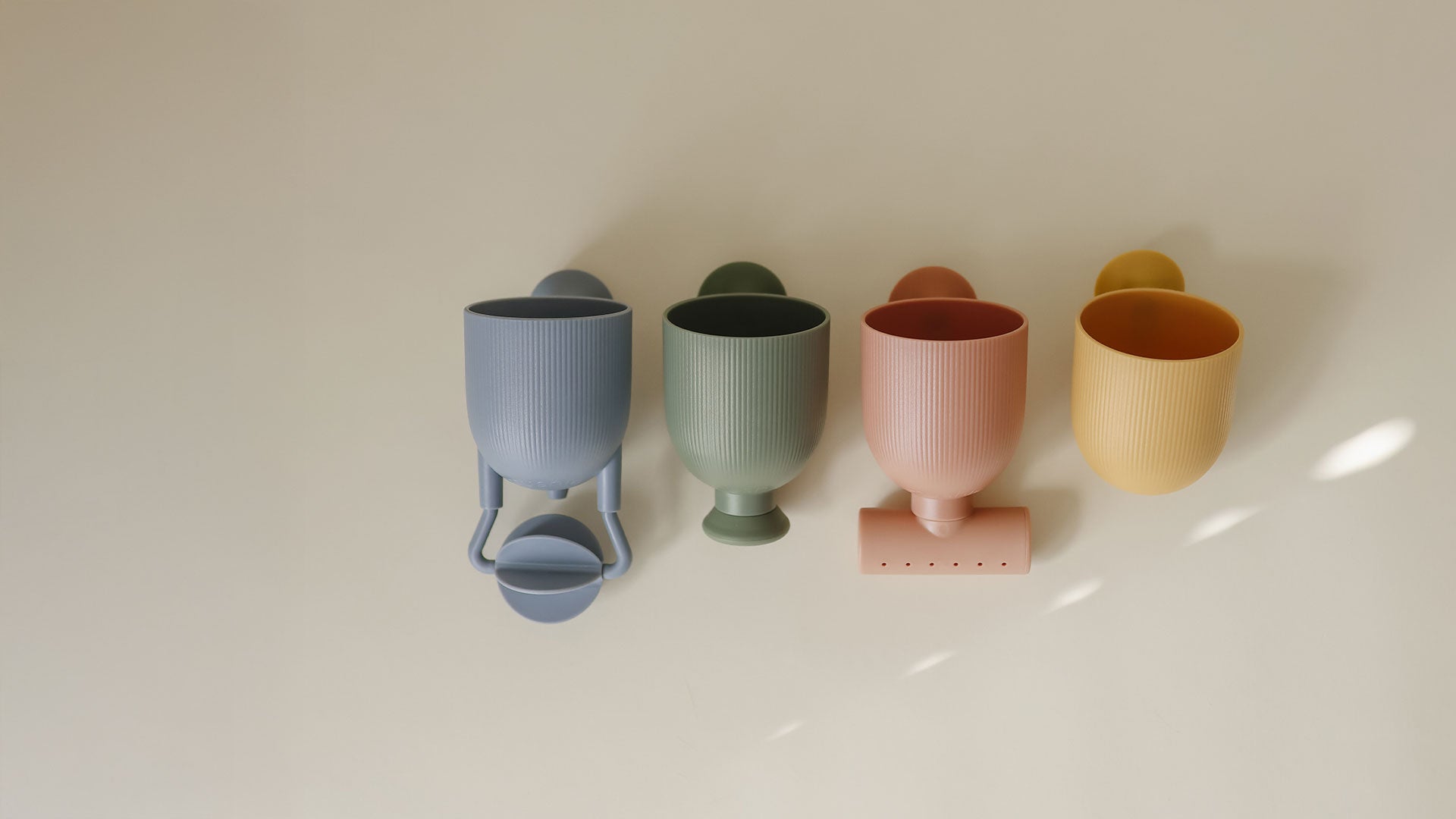 New bath pour and play set: Four ribbed cups in muted pastel colors including blue-gray, sage green, dusty pink, and mustard yellow, arranged on a plain light beige surface.