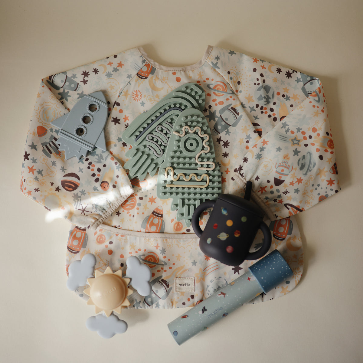 Mushie Silicone Sensory Toy for fine motor play on beige background with space-themed items.