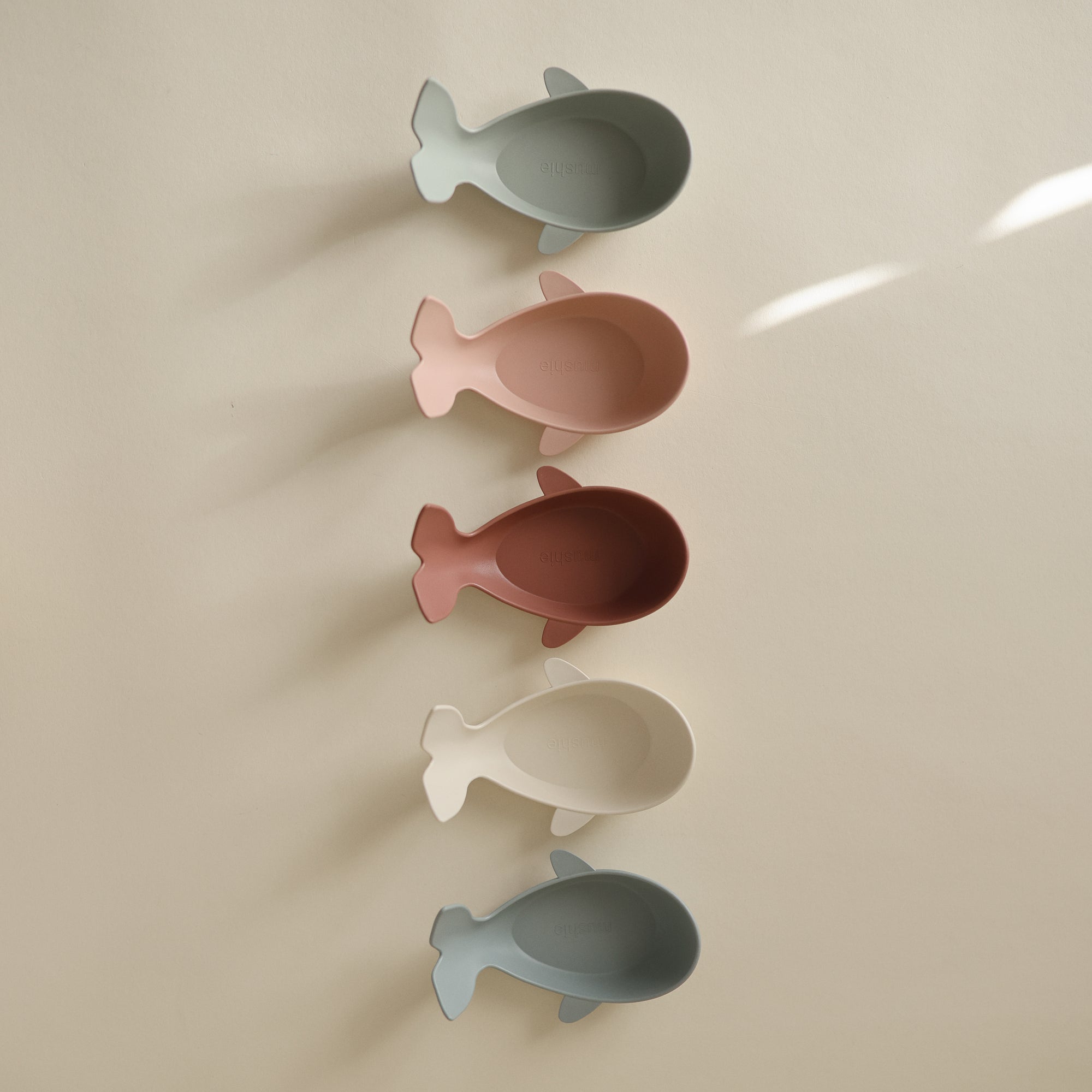 Five pastel Whale Bath Stackers by Mushie stacked vertically on a light surface.