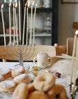 A lit menorah, donuts, and gelt sit by a mushie Silicone Baby Bib for Hanukkah fun.