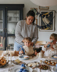 Mom with two kids at a festive table; one wears mushie’s colorful Silicone Baby Bib.