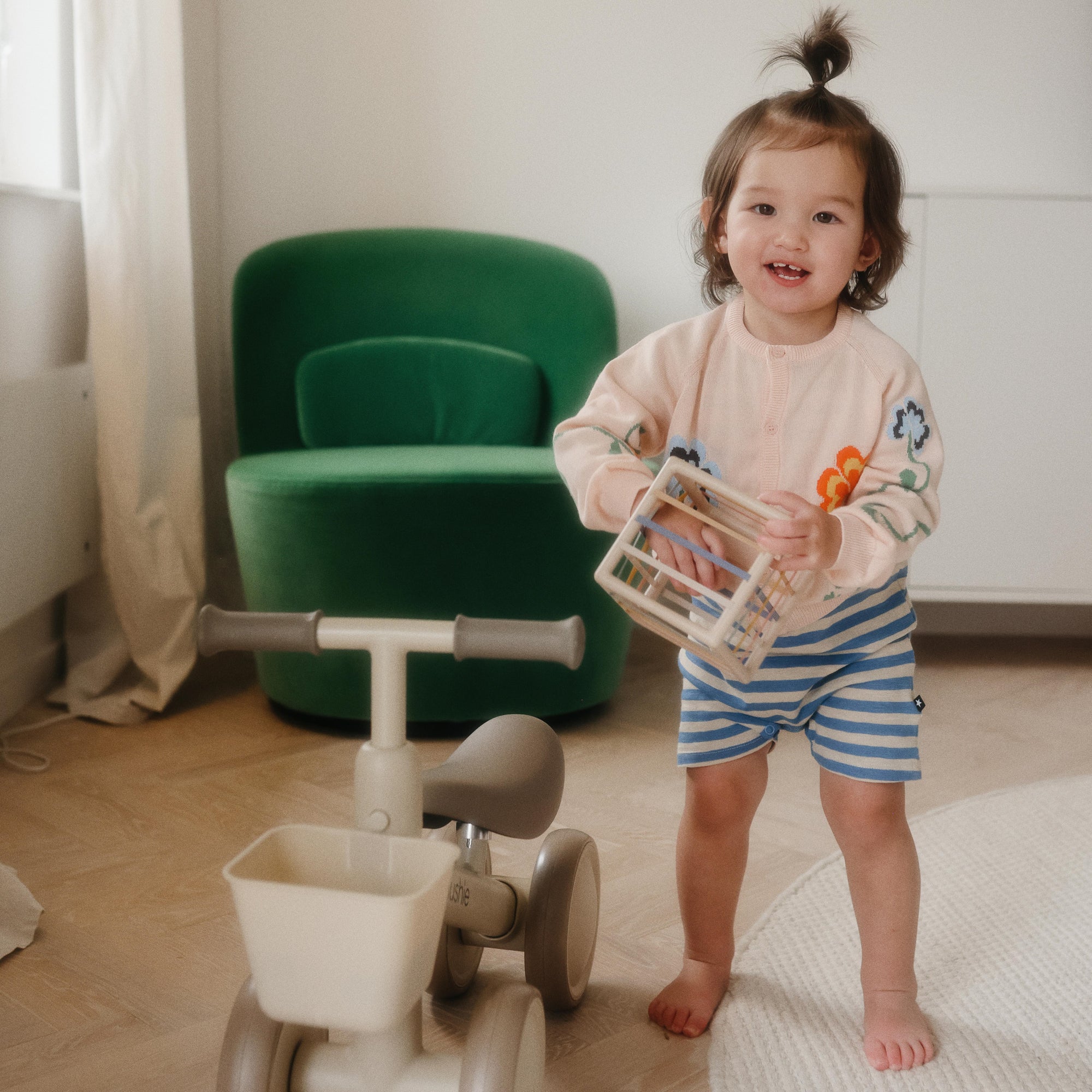 Smiling toddler plays with mushie's Elastic Shape Sorter, building fine motor skills.