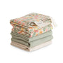A neatly stacked pile of mushie Muslin Cotton Washcloths features two floral-patterned cloths on top and three solid green and beige organic cotton muslin washcloths underneath, all set against a white background.