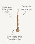 The mushie Silicone Pacifier Clip | Hera features a minimalist design with food-grade silicone beads and a wooden clasp. Free of BPA, BPS, PVC, and phthalates—ideal for on-the-go use.
