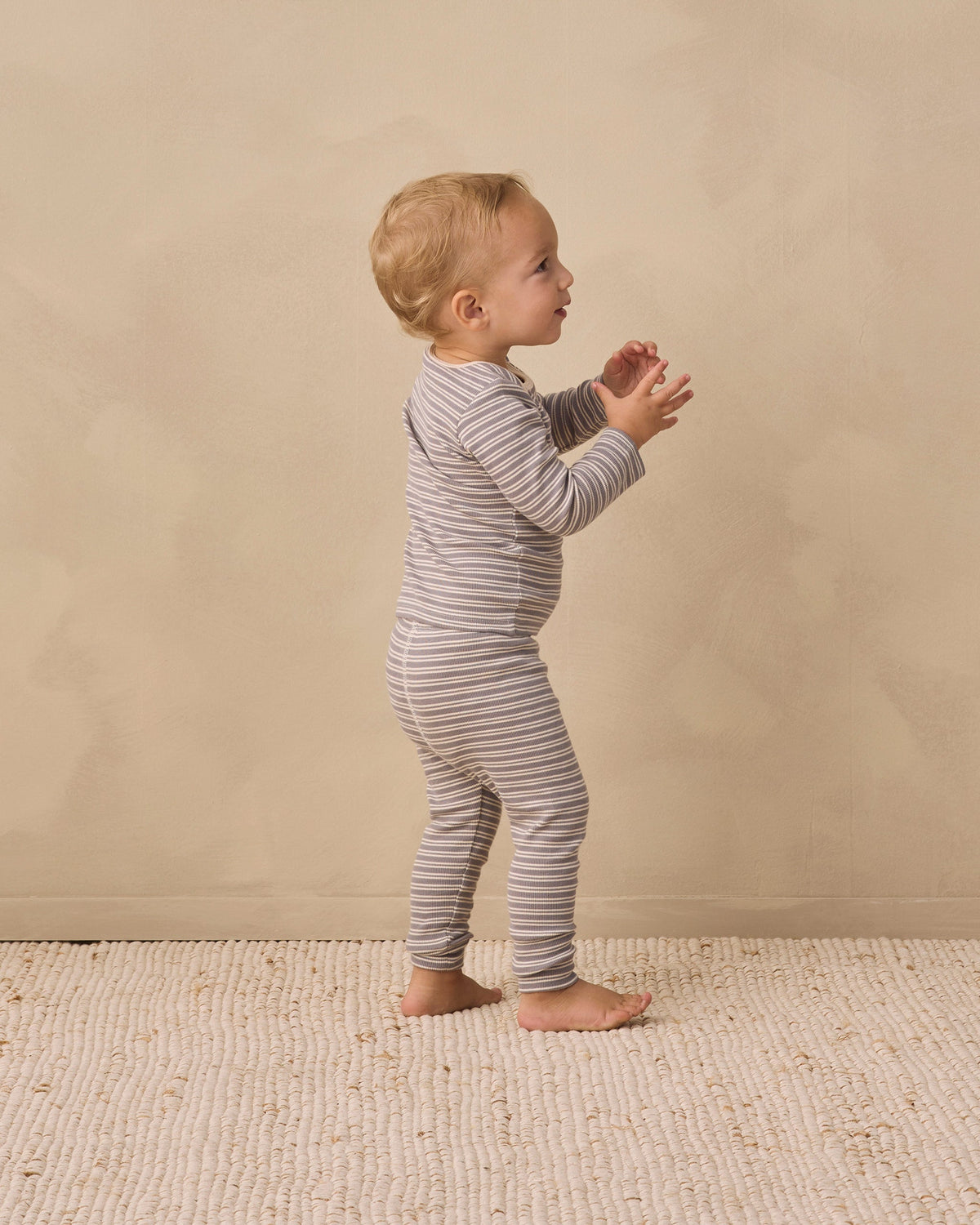 Toddler in Rylee + Cru Ribbed Tee + Legging Set Slate Microstripe stands on a beige rug.