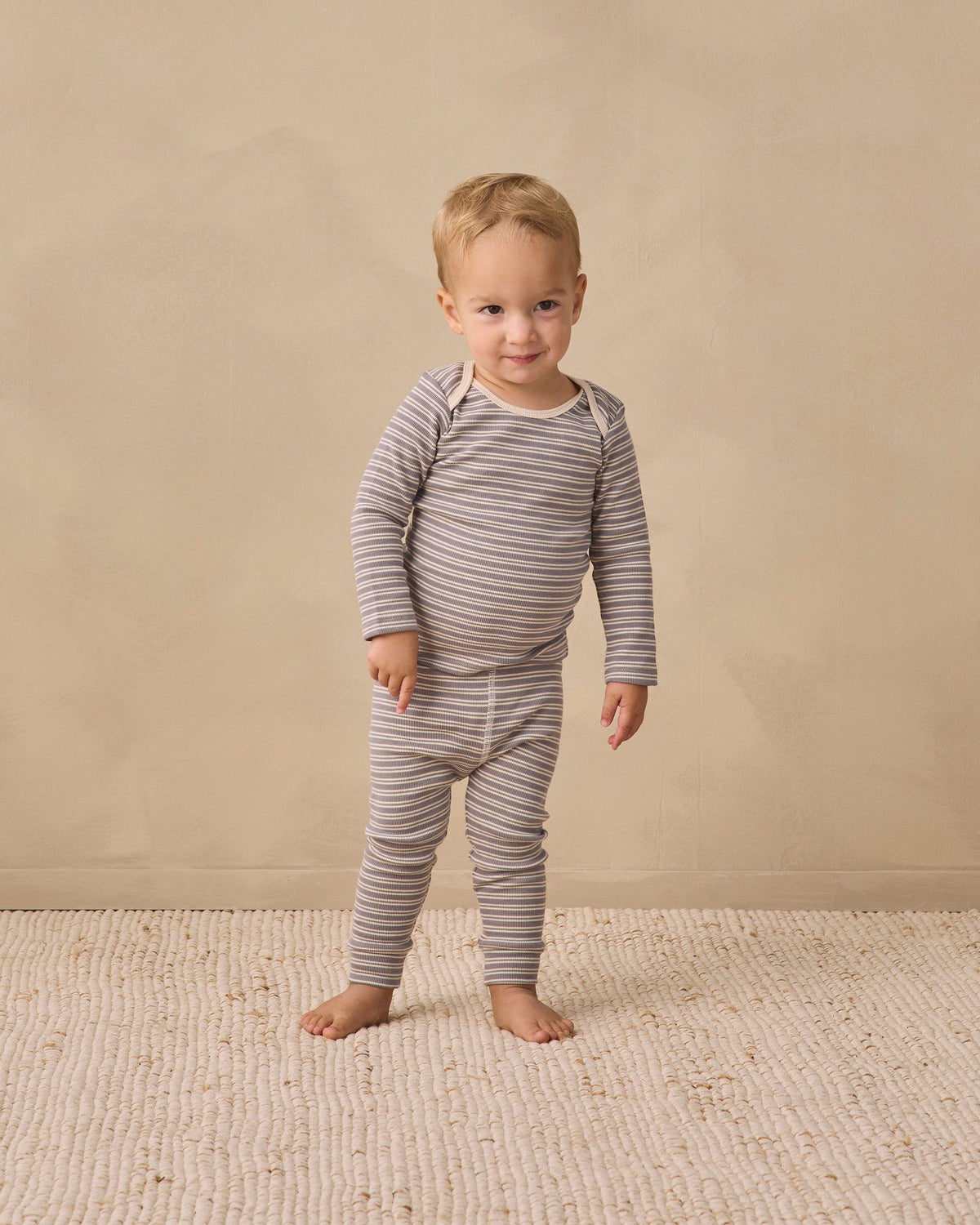 Toddler in Rylee + Cru Ribbed Tee + Legging Set Slate Microstripe stands barefoot on a rug.