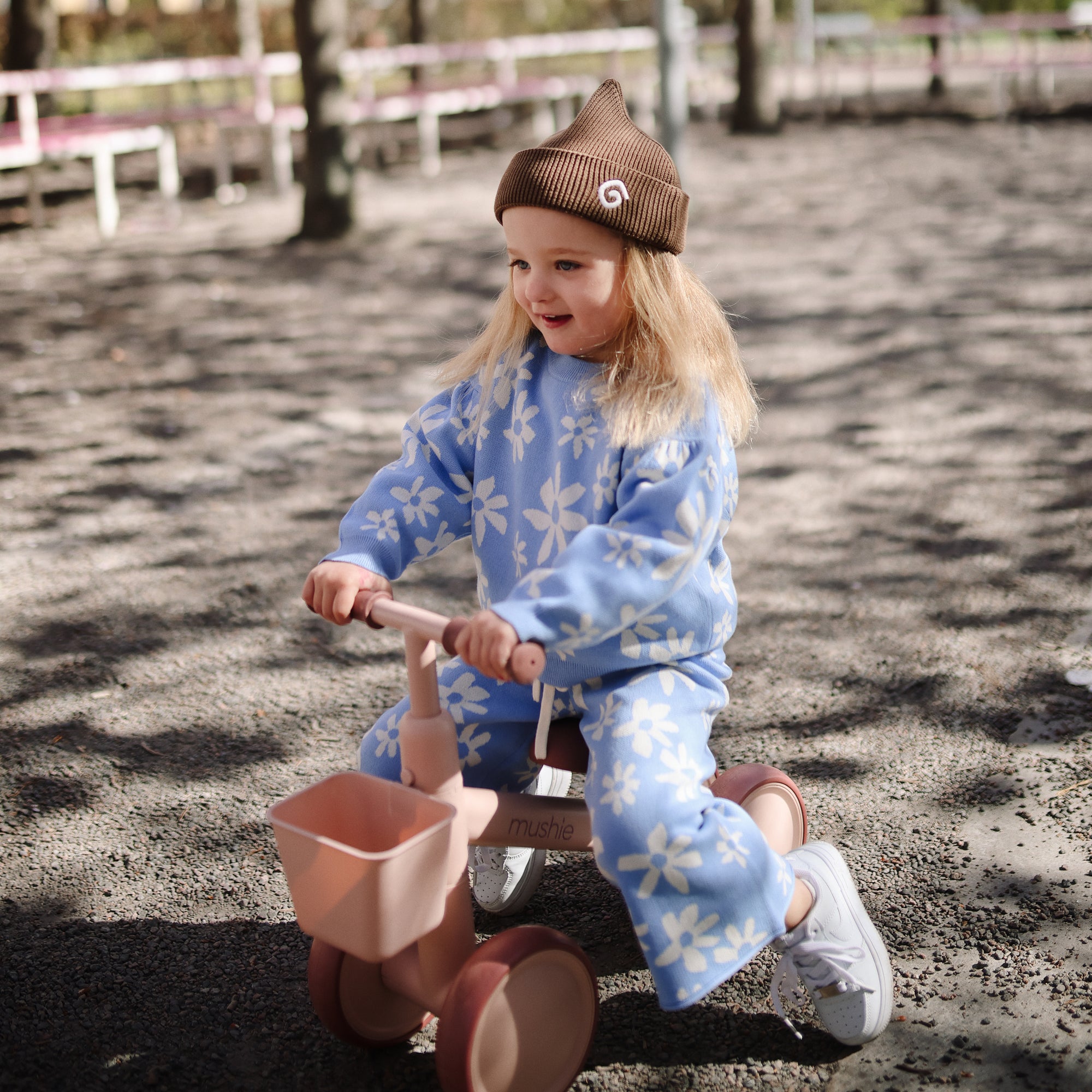 Smiling toddler in mushie Mini Toddler Bike and blue flower outfit rides outdoors for first time.