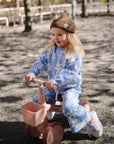 Smiling toddler in mushie Mini Toddler Bike and blue flower outfit rides outdoors for first time.