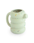 Mushie silicone watering can in light green with a tiered body and colorful confetti speckles.