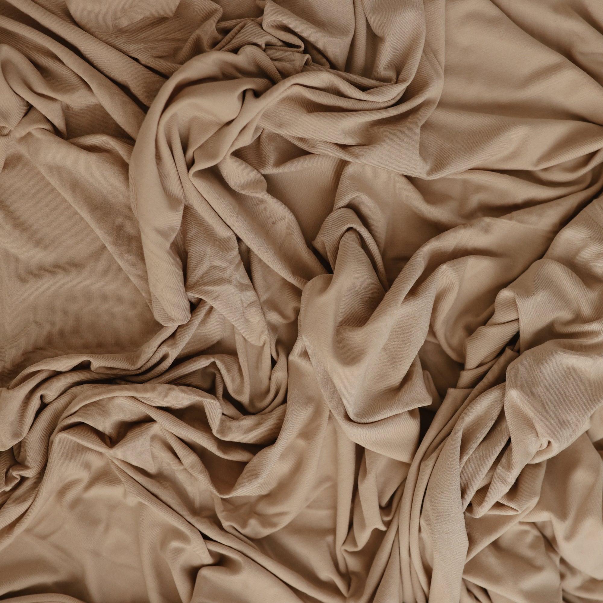 The mushie Stretchy Swaddle in beige features breathable, soft fabric with a textured, layered look from natural folds and creases—perfect for keeping your baby cozy and comfortable.