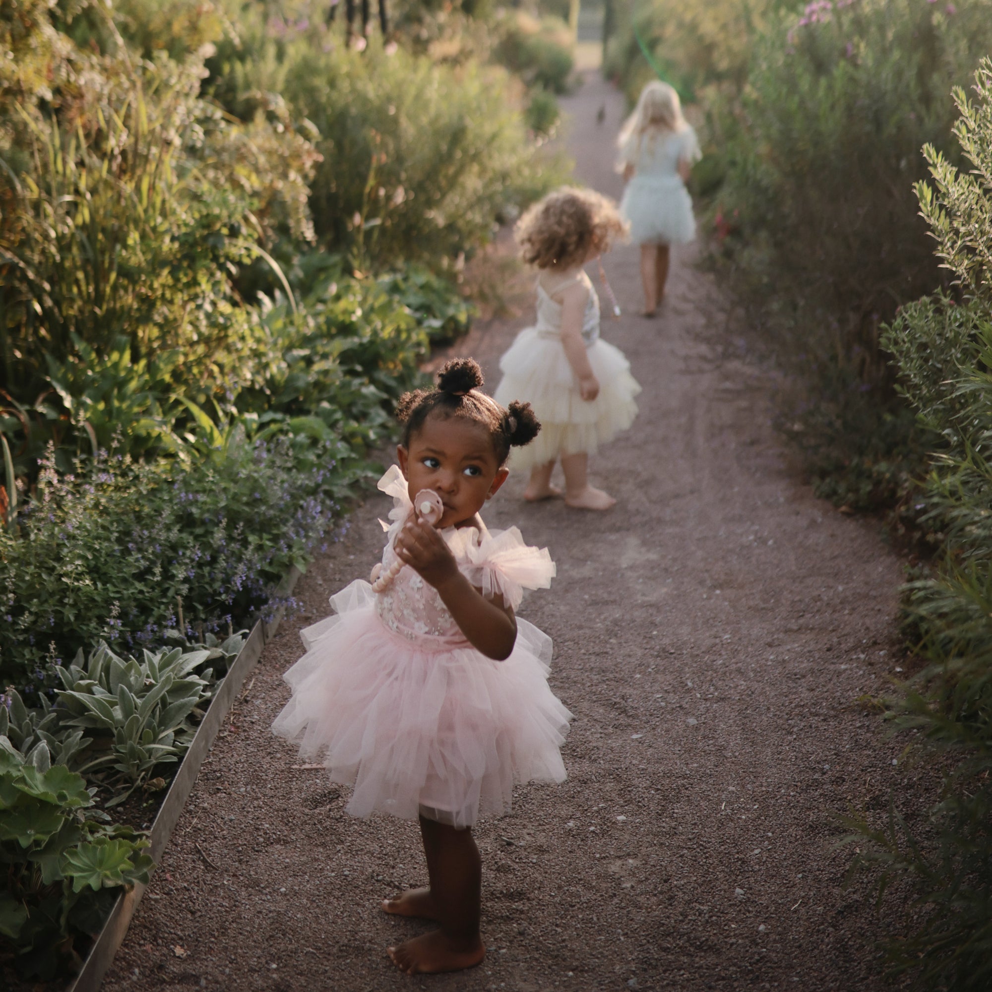 Young girls play barefoot; one drinks, holding a FRIGG Daisy Natural Rubber Pacifier.
