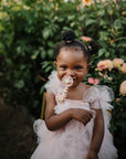A young girl smiles in the garden, holding a FRIGG Daisy Natural Rubber Pacifier.