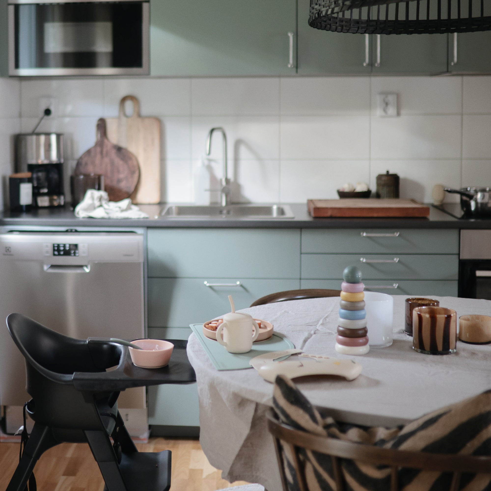 Modern kitchen with green cabinets, Danish Hygge style, and a mushie Stacking Rings Toy on the table.