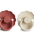 The FRIGG Daisy Natural Rubber Pacifier 2-Pack includes two pacifiers in muted red and cream, both with scalloped daisy edges, round handles, identical designs, and natural rubber latex nipples for baby's comfort.