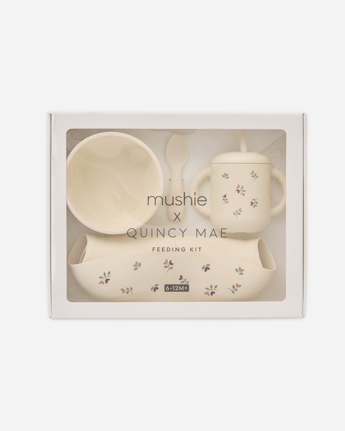 Mushie x Quincy Mae Feeding Kit in a white gift box with a clear window, containing a cream-colored bowl, sippy cup with straw, spoon, and small footmuff.
