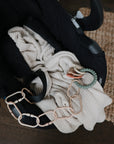 Black baby car seat with a cream blanket and mushie Teething Ring on a wooden floor and rug.