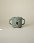 Mushie Snack Cup—green, spill-proof, handles, Christmas tree design; ideal for toddlers.