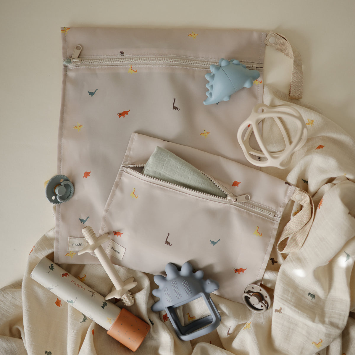 Two mushie Water Resistant Wet bags surrounded by baby teethers and pacifiers.