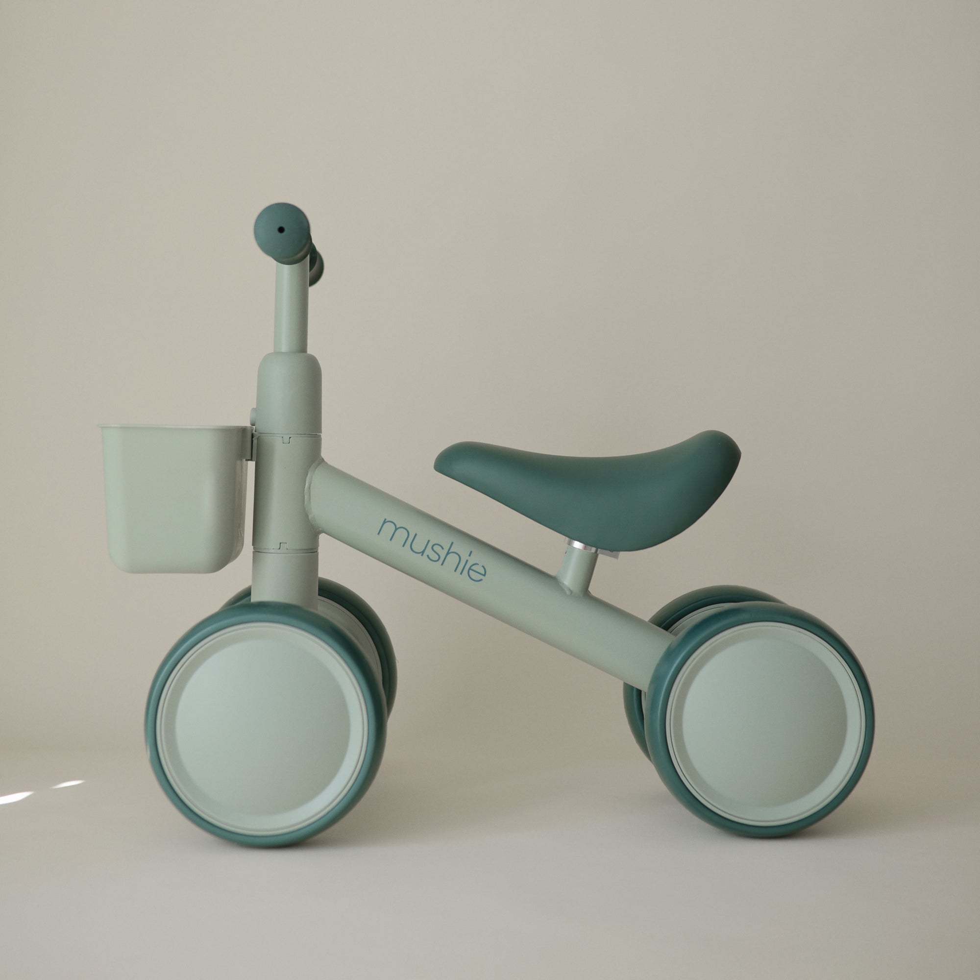 Mushie Mini Toddler Bike in mint green with front basket, shown on a beige background.