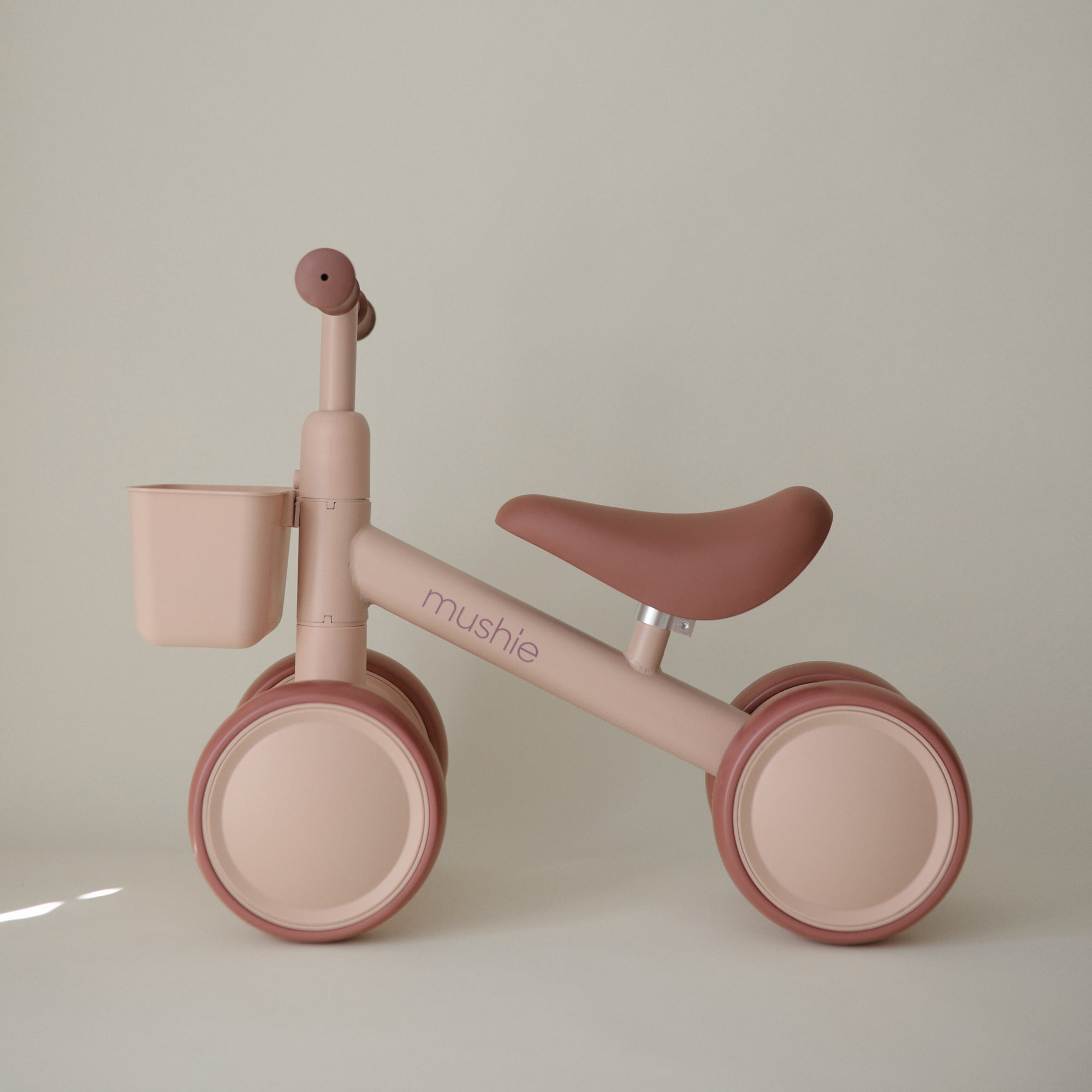 The mushie Mini Toddler Bike in beige and pink has a front basket—great as a first bike.